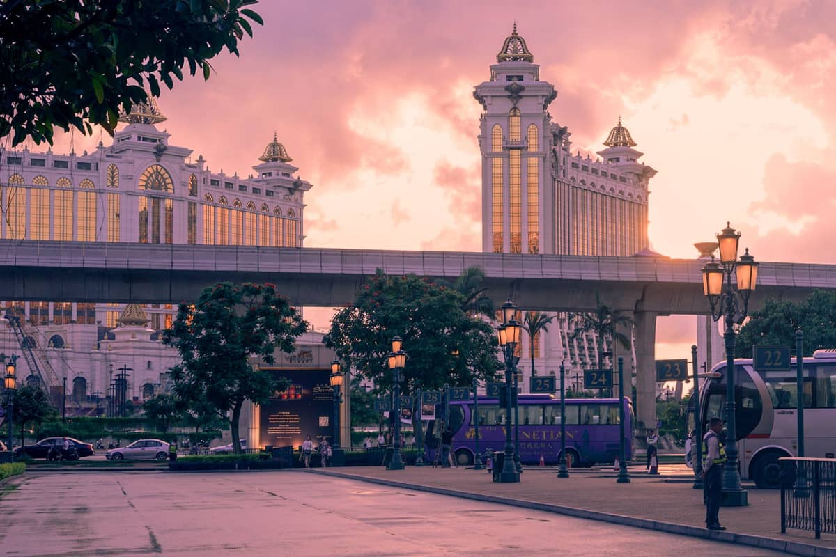 Busse warten bei Sonnenuntergang vor dem Casino-Resort Galaxy Macau, mit sichtbaren Bushaltestellen und Menschen, die den Shuttle-Transport des Casinos hervorheben.