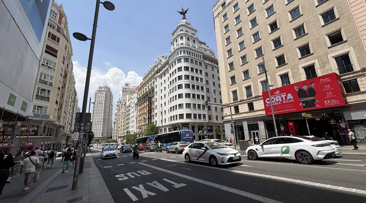 Belebte Stadtstraße in Madrid mit weißen Taxis mit rotem Streifen, Stadtsehenswürdigkeiten und einer eigenen Taxispur, die lokale Transportmöglichkeiten zeigt.