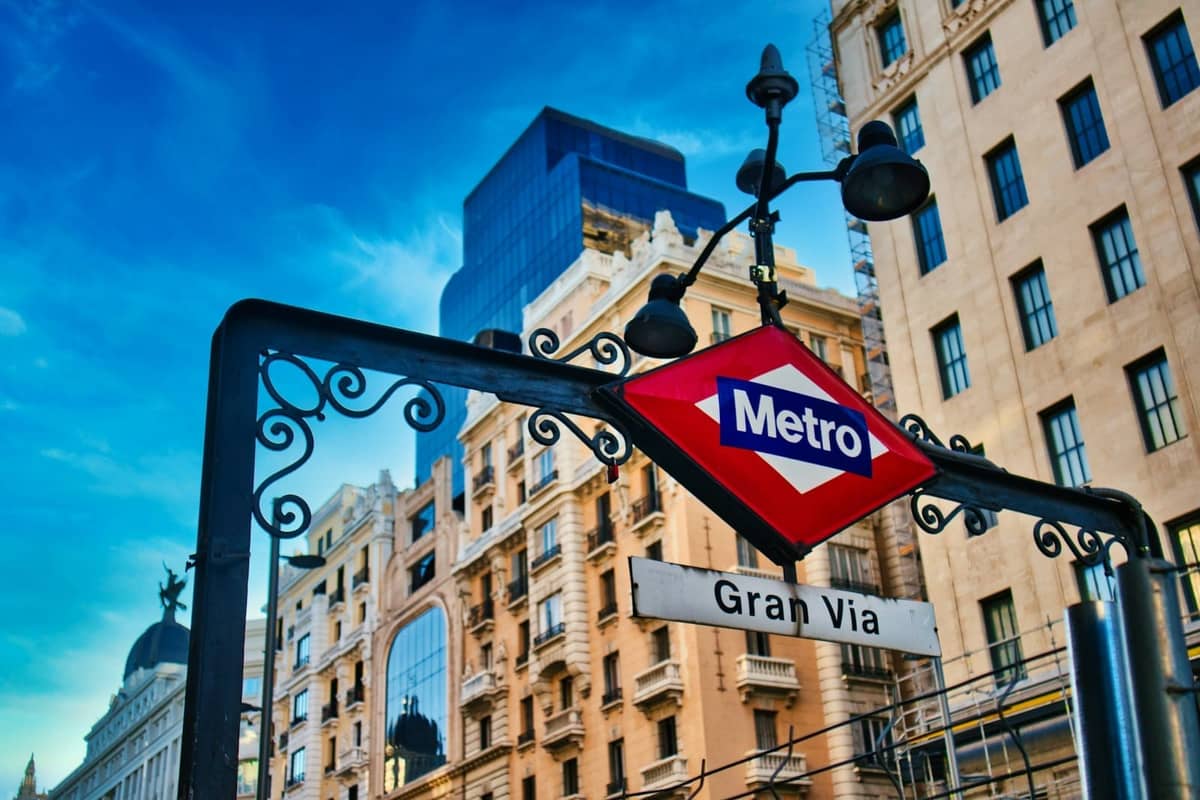 Metro Madrid-Schild der Station Gran Vía mit historischen Gebäuden im Hintergrund an einem strahlend sonnigen Tag.