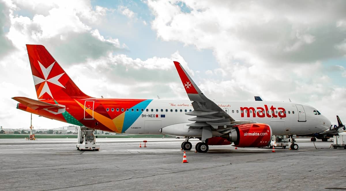 Aereo di Air Malta parcheggiato sul piazzale dell'Aeroporto Internazionale di Malta con carrelli portabagagli e chiara vista del marchio dell'aeromobile.
