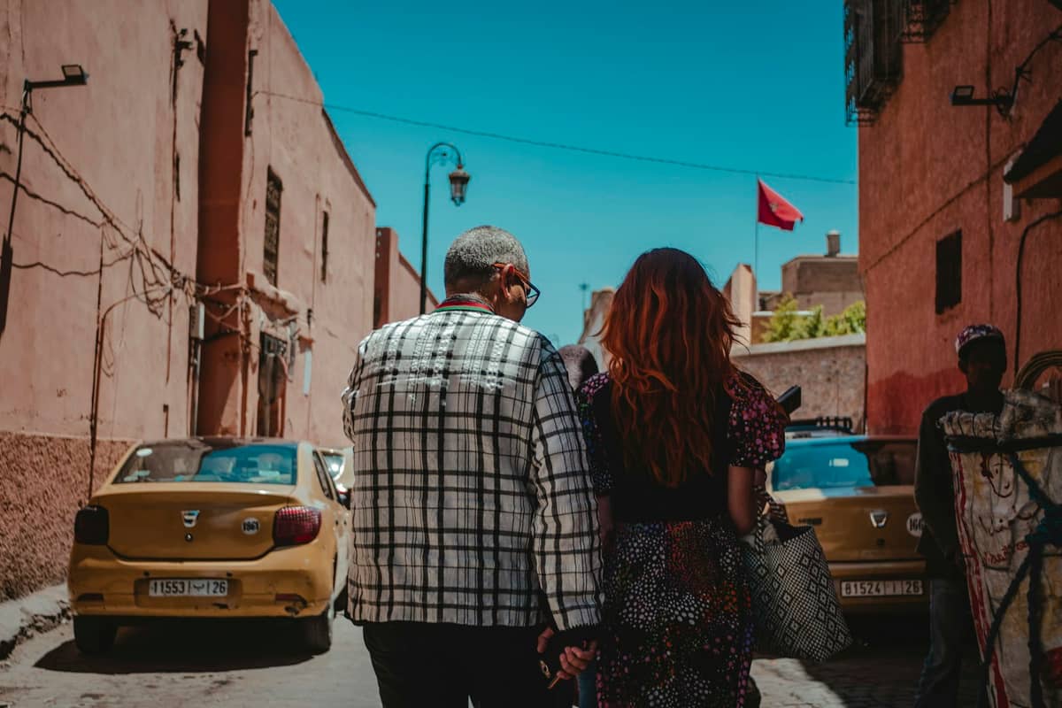 แท็กซี่สีเหลืองสองคันจอดอยู่บนถนนแคบๆ ในเมือง Marrakech ขณะที่คู่รักเดินจากไปในเวลากลางวัน