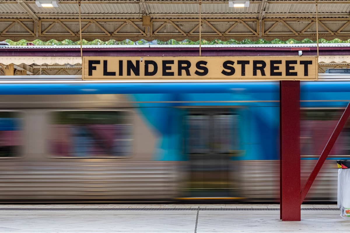 A metropolitan train speeds past the Flinders Street station platform sign inside Melbourne’s central railway hub.