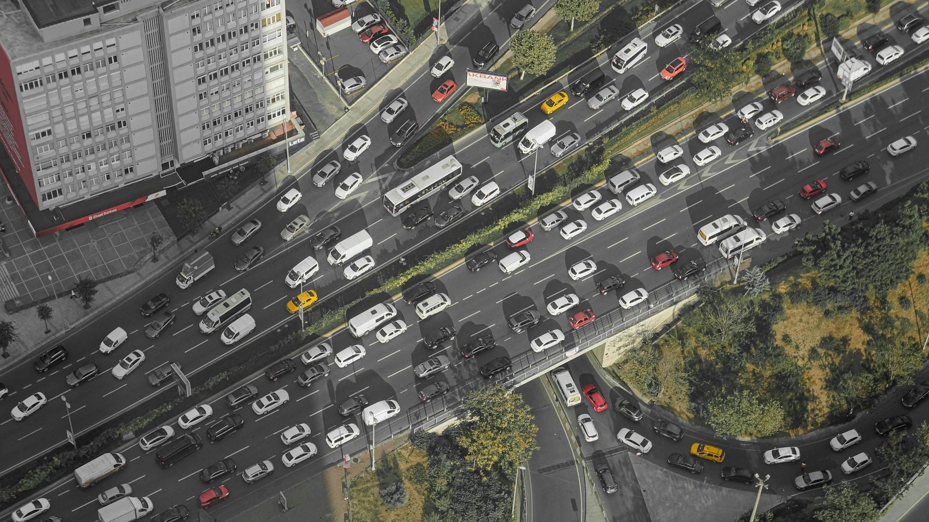 Vista aérea de tráfego intenso e congestionamento em uma rua principal da cidade com muitos veículos cercados por edifícios urbanos e vegetação.