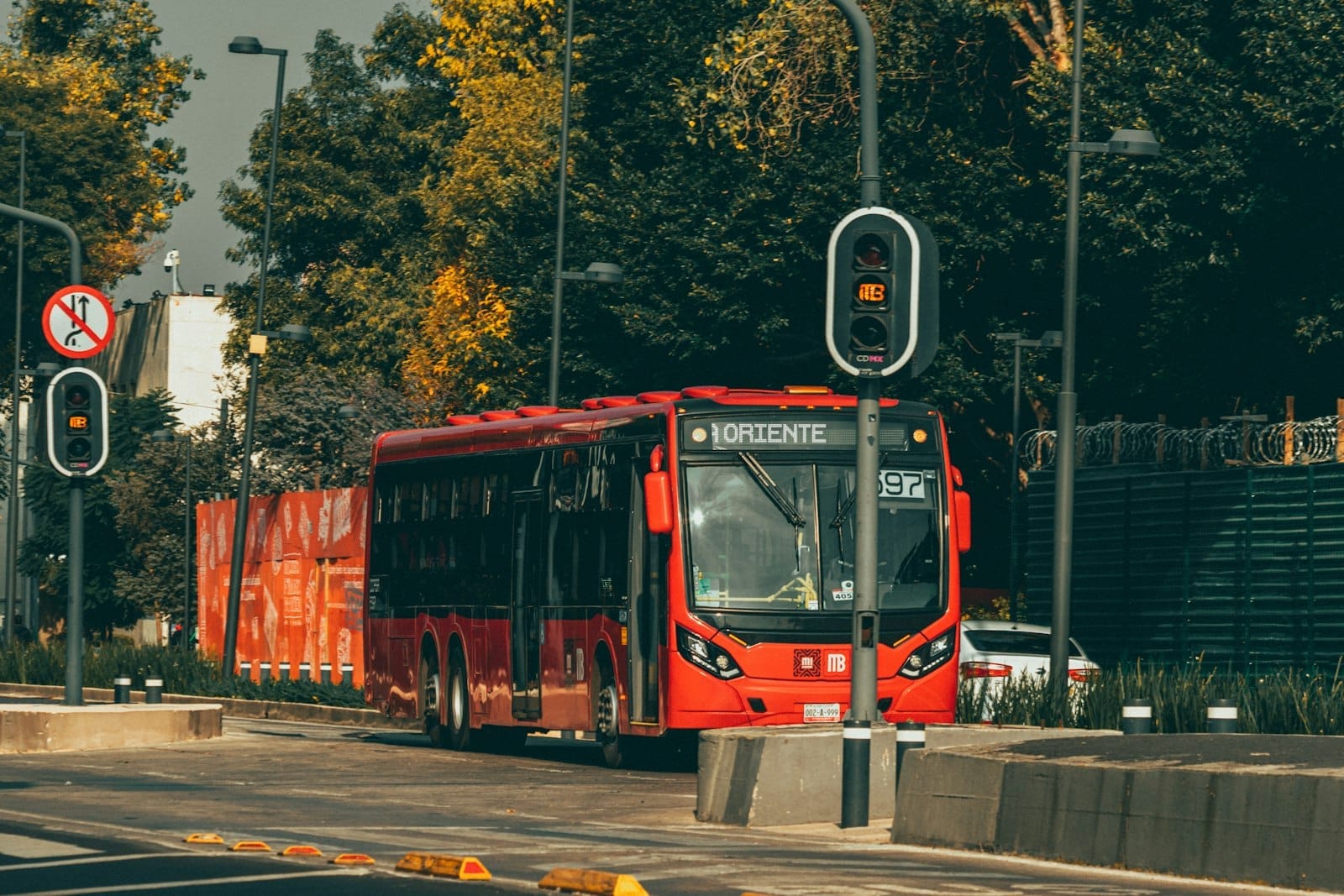 Um Metrobús vermelho trafegando por uma faixa exclusiva na Cidade do México, com árvores e infraestrutura urbana ao fundo.