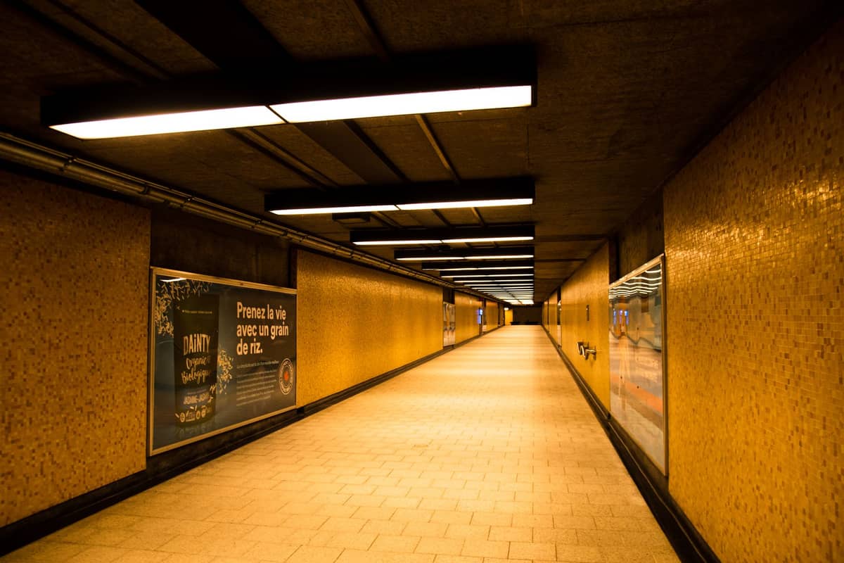 A long underground pedestrian corridor with yellow-tiled walls, bright overhead lights, and posters along the sides.
