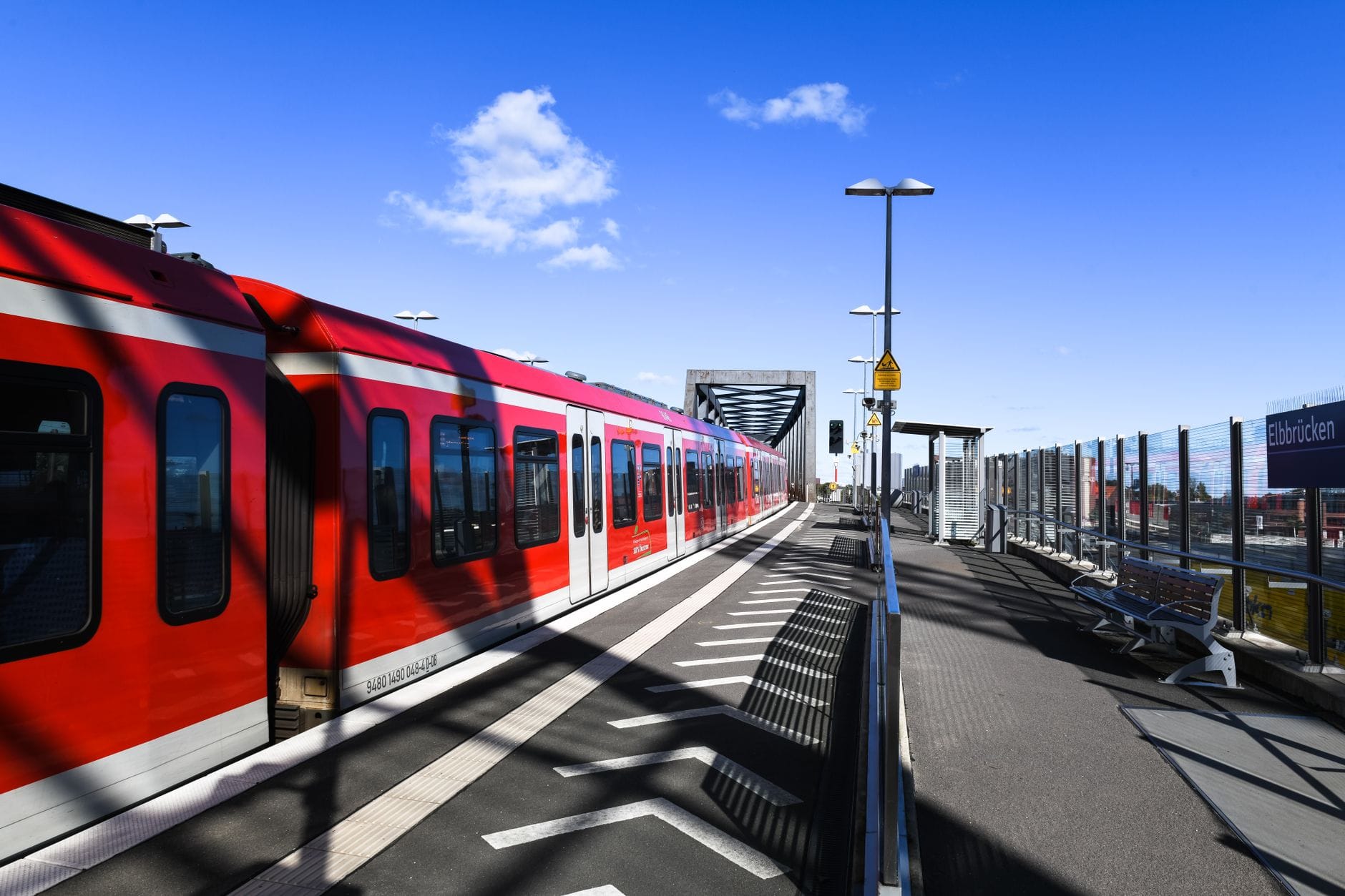 รถไฟ S-Bahn สีแดงที่ชานชาลาสถานีกลางแจ้งในมิวนิกใต้ท้องฟ้าสีฟ้าแจ่มใส