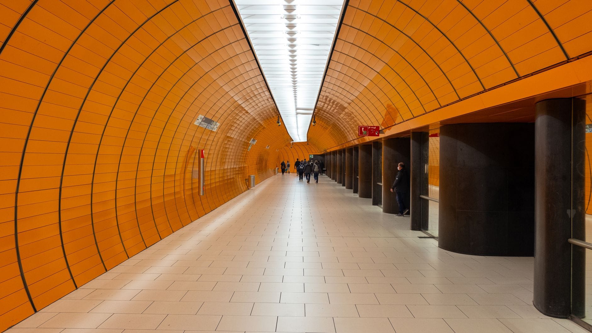 วิวกว้างของทางเดินที่โดดเด่นด้วยกระเบื้องสีส้มภายในสถานี U-Bahn Marienplatz เมืองมิวนิก พร้อมผู้คนเดินอยู่ในระยะไกล