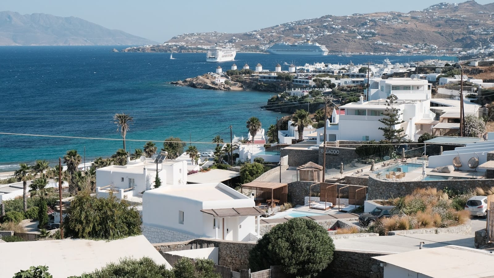 Vista panorámica de la costa de Mykonos con edificios blancos, crucero y ferrys llegando al puerto.