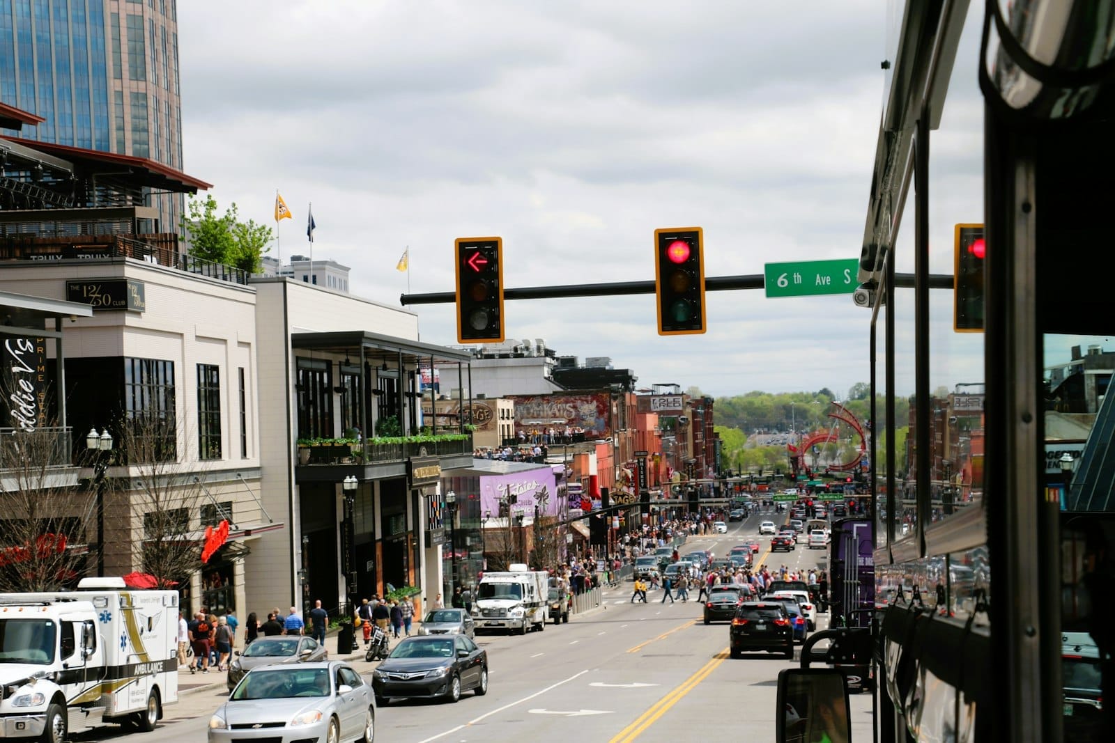Calle animada de Nashville con coches, autobuses y peatones bajo semáforos y edificios urbanos, reflejando la variedad de opciones de transporte en la ciudad.