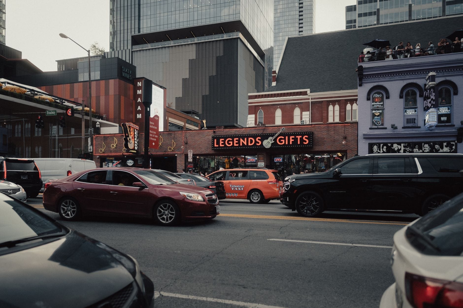 Vista de una calle en el centro de Nashville con coches y un taxi en el tráfico, con edificios locales reconocibles y luces de neón.