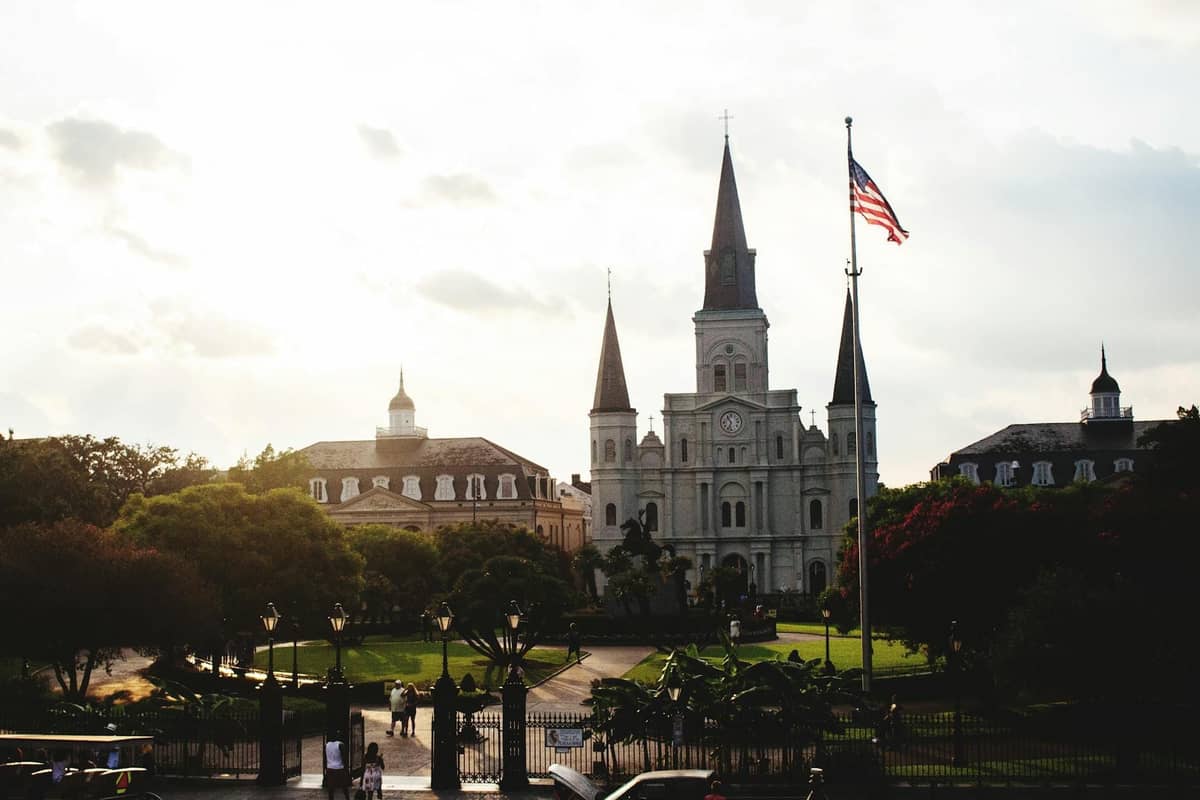 Iconic view of St. Louis Cathedral with Jackson Square in foreground, people walking along paths, and the American flag in New Orleans.