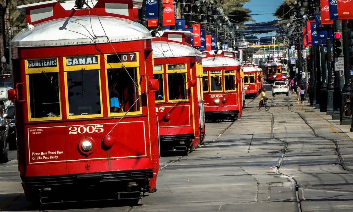 Multiple classic red New Orleans streetcars lined up on Canal Street, palm trees and banners visible, offering a lively city transport scene.