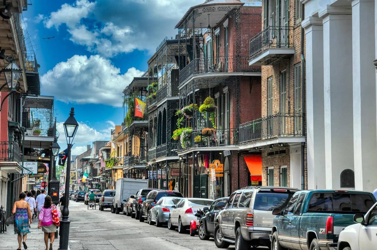 People walking along a lively, historic street in New Orleans with iconic balconies and colorful buildings.