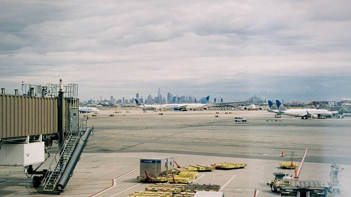 Flughafenlandebahn mit Flugzeugen und einem fernen Blick auf die Skyline von New York City unter bewölktem Himmel.