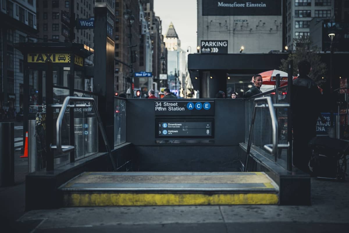 Straßenebener Eingang zur U-Bahn-Station Penn Station an der 34th Street mit sichtbaren Linien A, C, E und New Yorker Gebäuden im Hintergrund