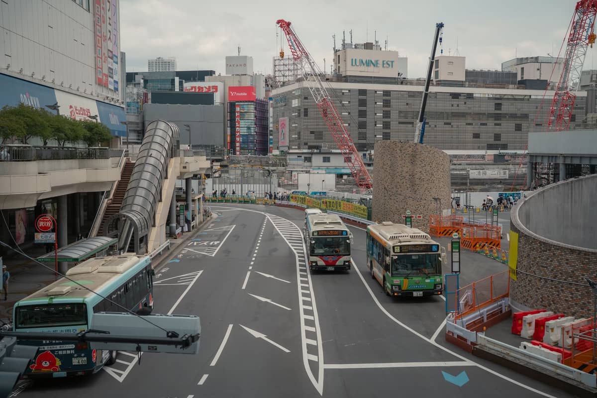 City buses parked along a dedicated bus lane in a modern urban Osaka setting with department stores and cranes in the background.