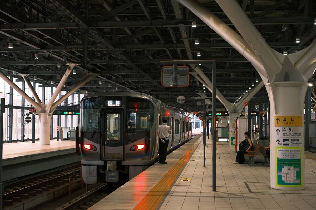 Modern train at a well-lit Osaka urban railway platform, with station staff and travelers nearby, showing the efficient public transport network.
