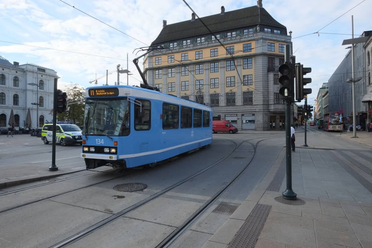 รถรางสีน้ำเงินของ Oslo วิ่งผ่านถนนในเมืองโดยมีอาคารเก่าแก่และทันสมัยเป็นฉากหลัง พร้อมสายไฟรถรางที่มองเห็นได้ด้านบน