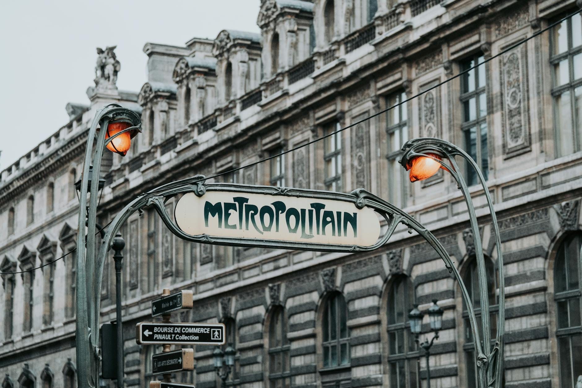 Jugendstil-Eingangsschilder der Pariser Métro mit kunstvollem Eisenwerk vor einer Kulisse klassischer Haussmann-Gebäude.