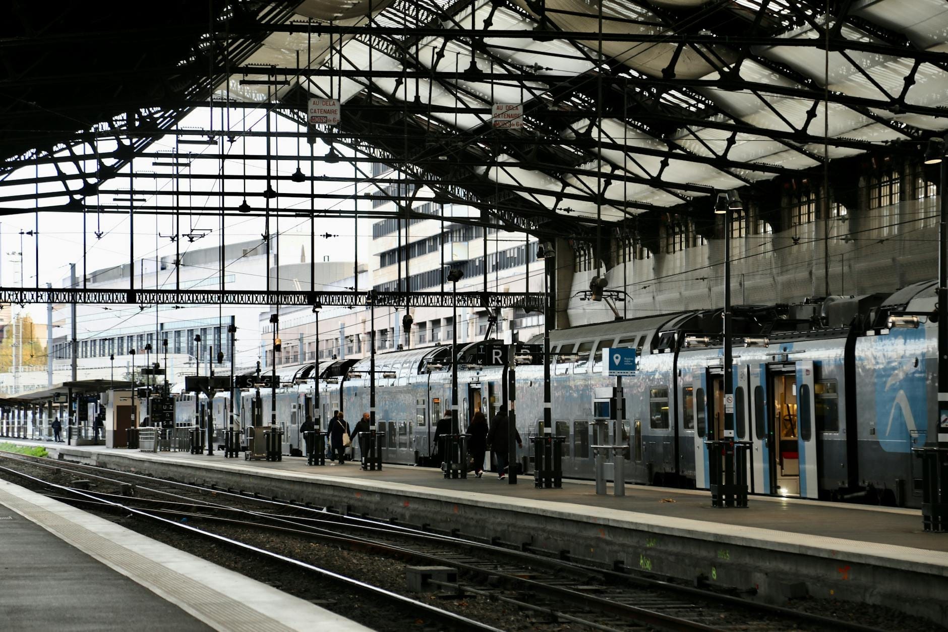 Überdachter Bahnsteig in einem Pariser Bahnhof mit Fahrgästen, die in einen modernen doppelstöckigen Regionalzug einsteigen.