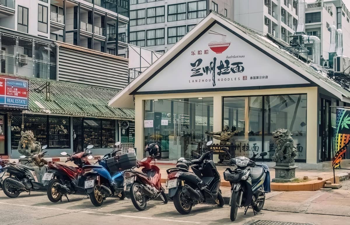 Several parked scooters and motorbikes in front of a storefront in a modern urban street in Pattaya.