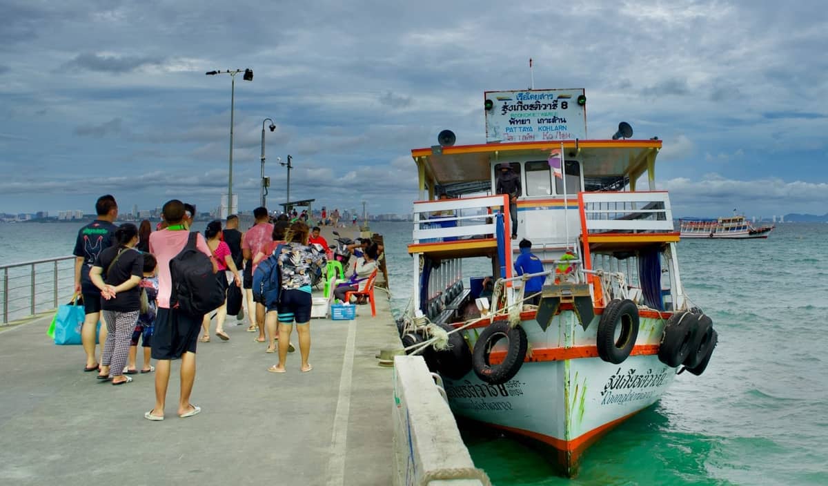 Travelers boarding a ferry at a Pattaya pier with the sea and boats in the background
