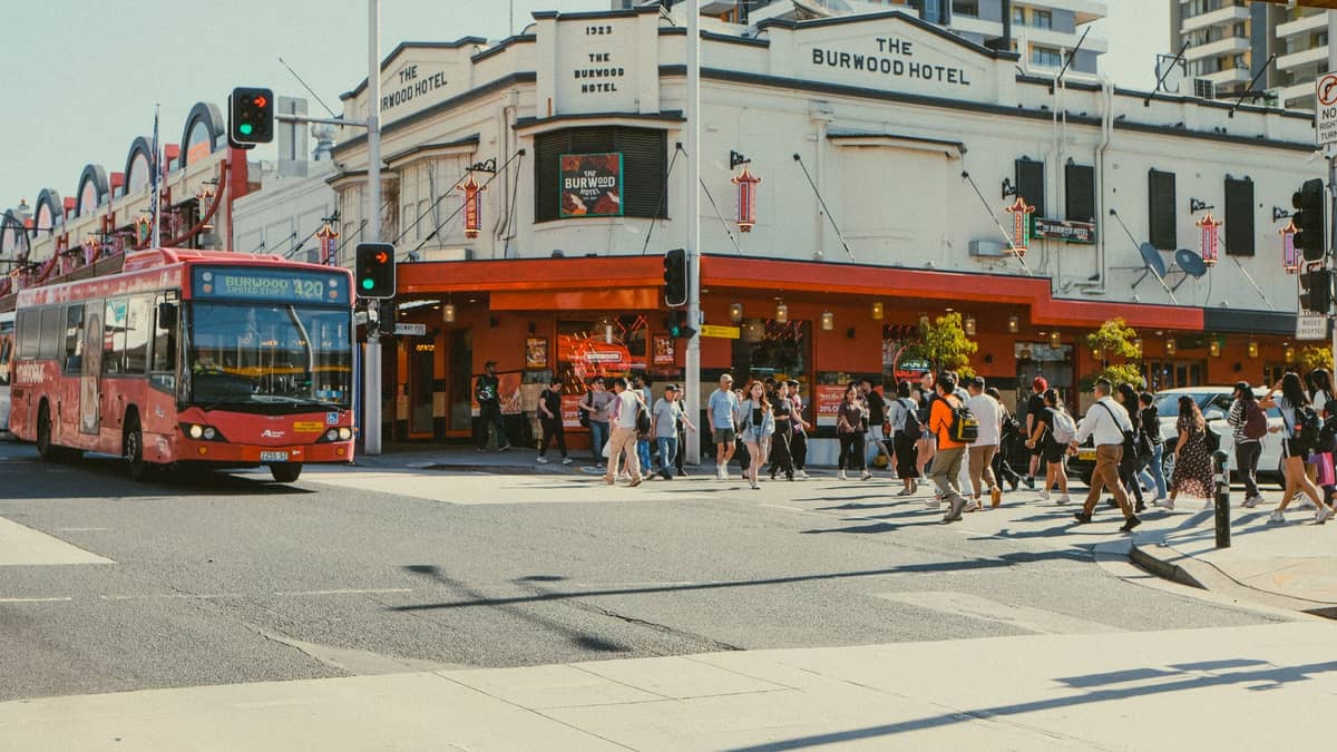 Ein roter Perth CAT Bus fährt am The Burwood Hotel vorbei, während eine Menschenmenge die Kreuzung im Stadtzentrum überquert.