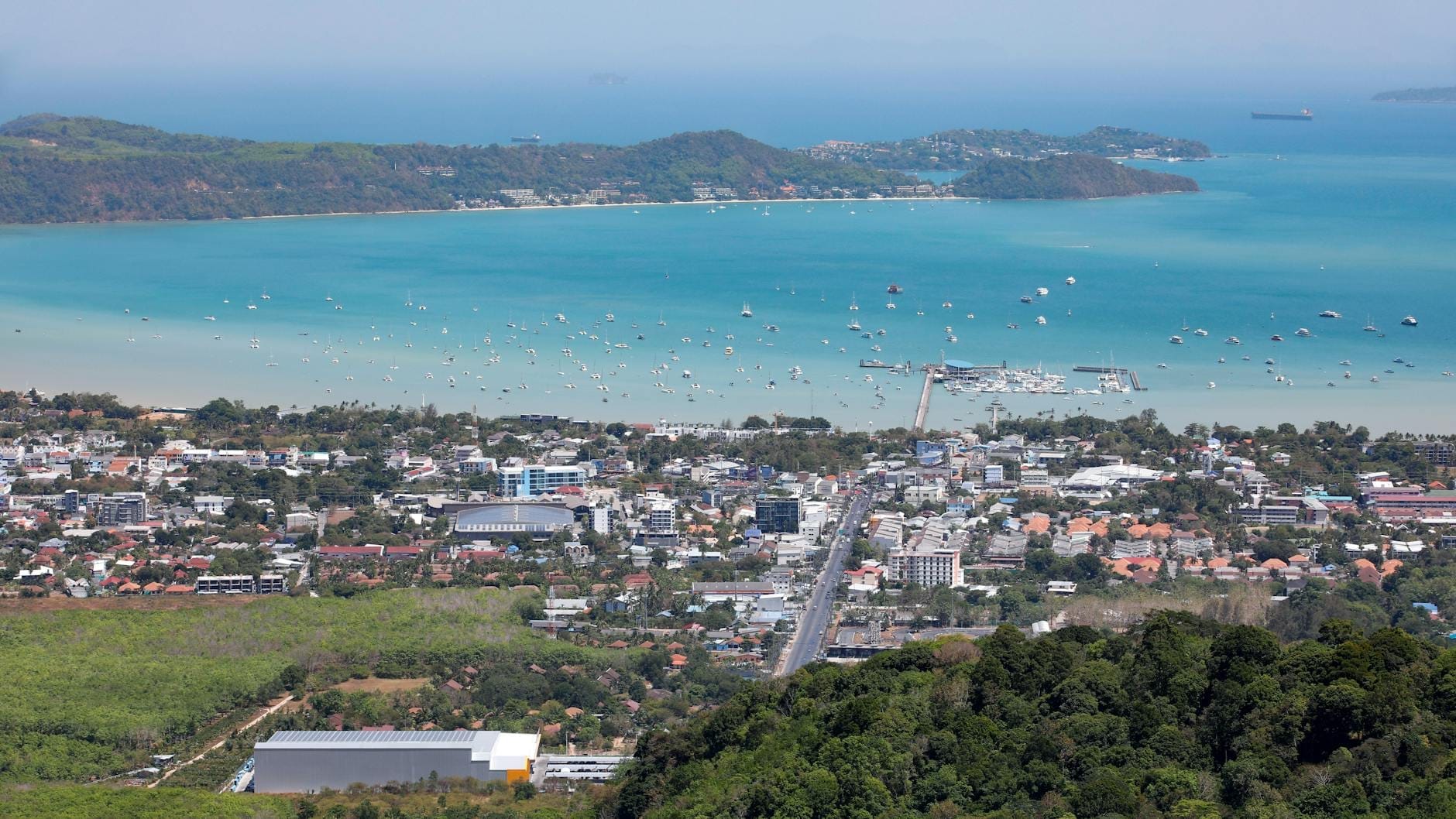 Aerial view of Phuket showing town, main road, coastline, and hilly terrain meeting the bay.