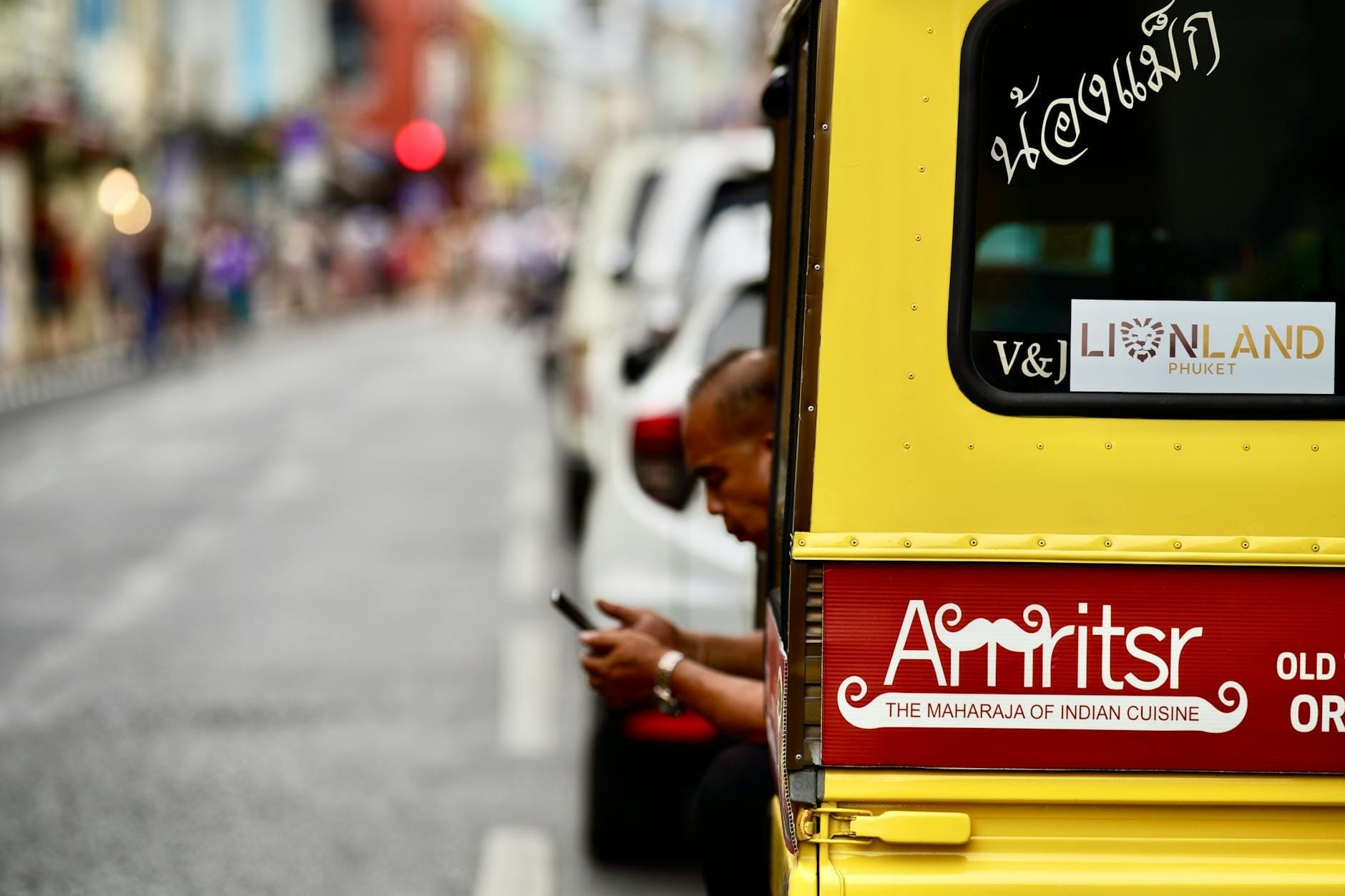 A yellow truck-style tuk-tuk with a man inside, parked on a street in Phuket's old town area.