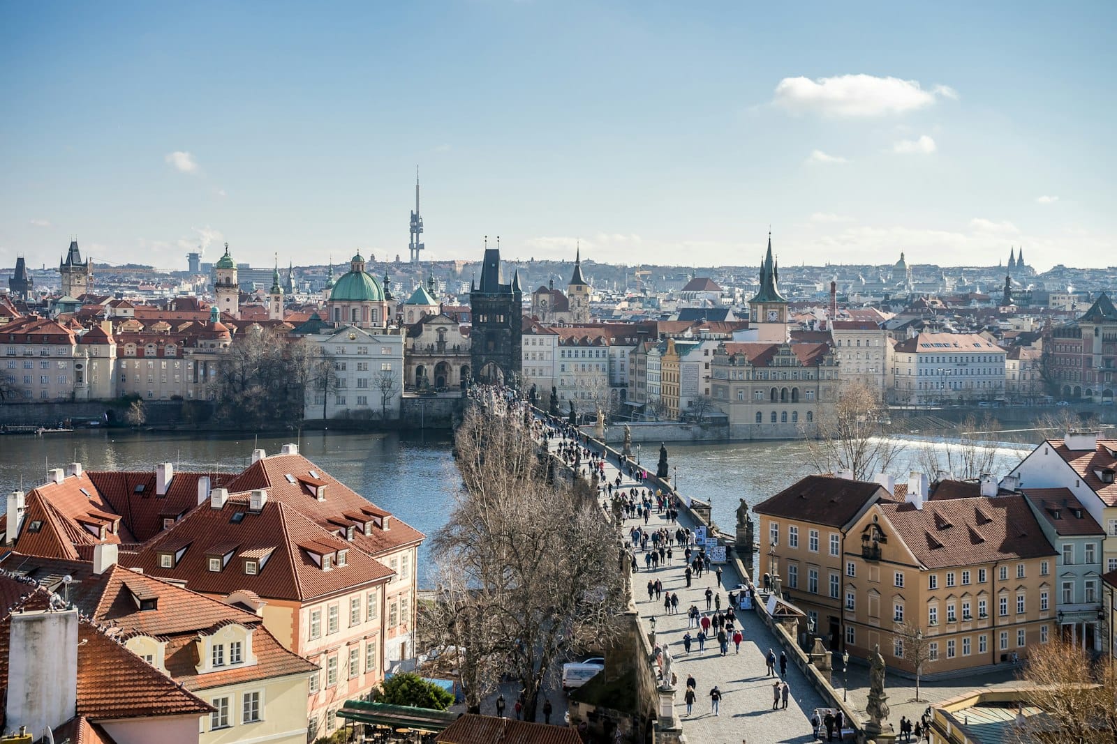 Vogelperspektive auf Prag mit der Karlsbrücke über der Moldau, Straßenbahnen und Stadtgebäuden an einem sonnigen Tag – Aufbruchstimmung und Bewegung pur.