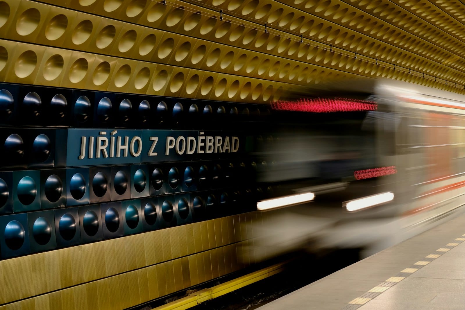 U-Bahn-Zug in Prag fährt in die Station Jiřího z Poděbrad ein, mit der charakteristischen gemusterten Wand und der Bewegungsunschärfe des Zuges.