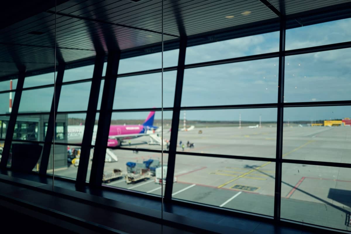 Fenster eines Flughafenterminals mit Blick auf das Vorfeld, wo ein Wizz Air-Flugzeug und Gepäckwagen zu sehen sind.