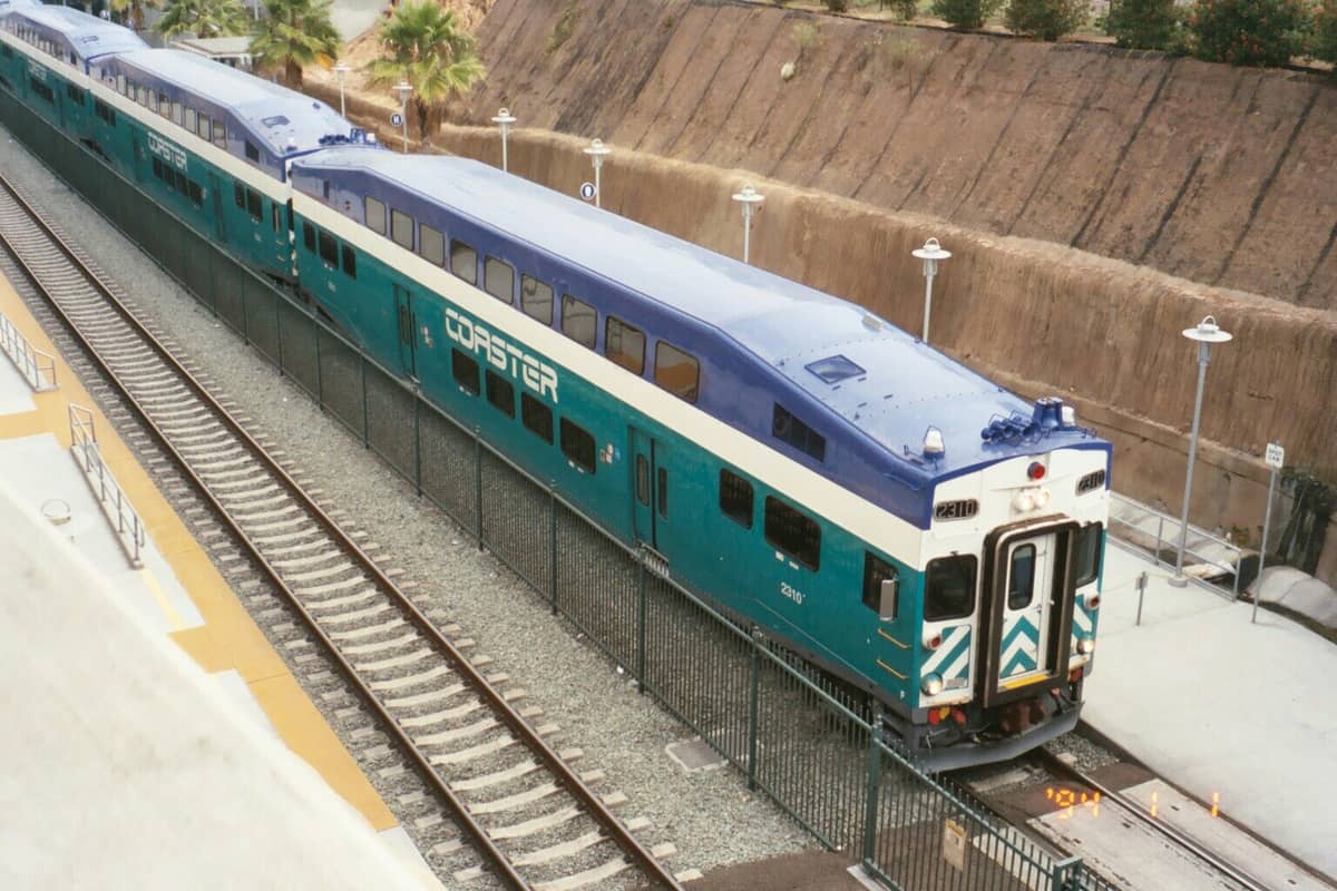 Blau-weißer COASTER-Pendlerzug an einem Bahnhof im San Diego County, mit sichtbaren Gleisen und Bahnsteigen.