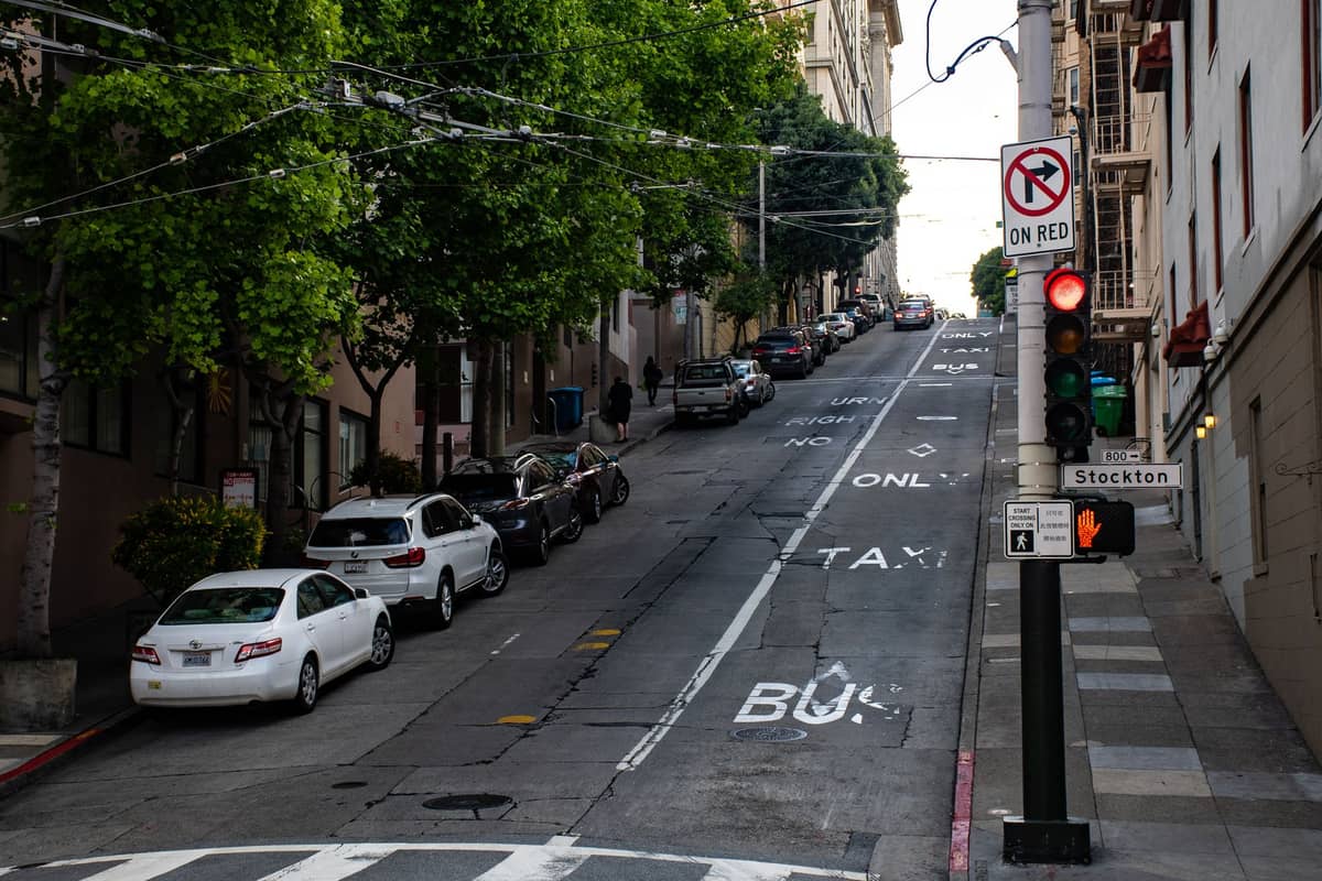 Steile Straße in San Francisco, gesäumt von geparkten Autos, Ampeln und einem Verbot-Rechtsabbiegen-Schild, das die schwierigen Fahr- und Parkverhältnisse in der Stadt veranschaulicht.