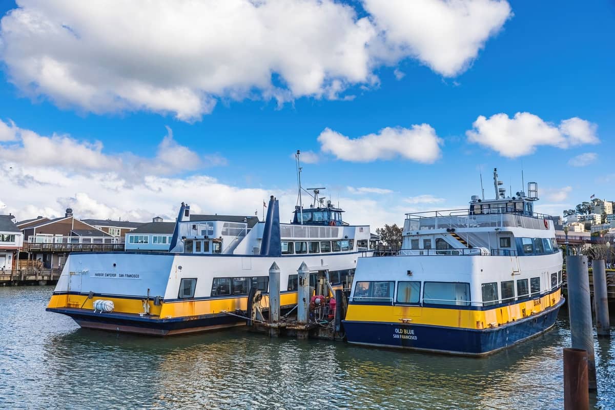 Zwei blau-gelbe Fähren an einem Pier am Ufer von San Francisco unter einem strahlend blauen Himmel mit vereinzelten Wolken.