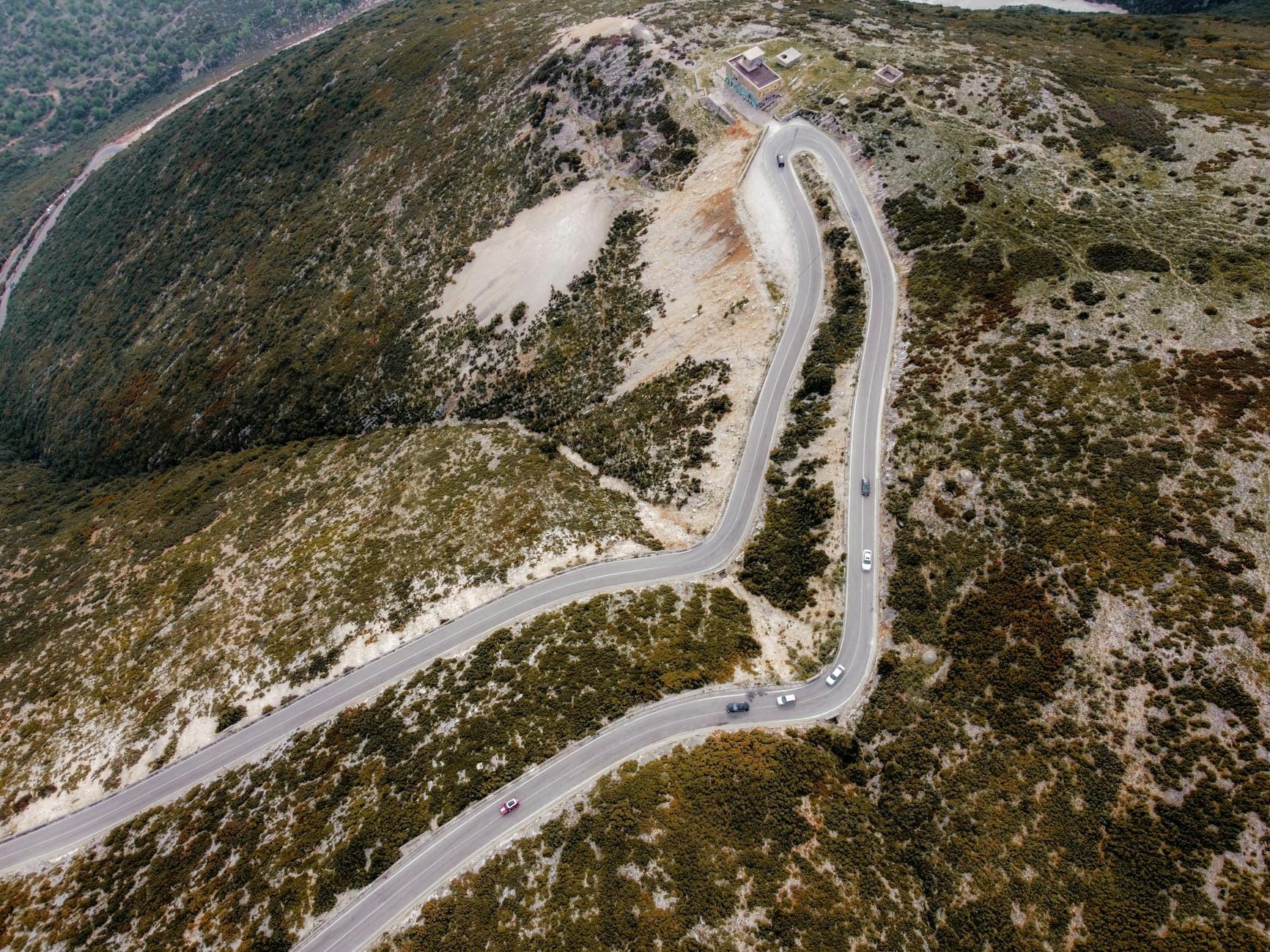 Luftaufnahme einer kurvenreichen, zweispurigen Bergstraße auf Sardinien mit wenig Verkehr und rauem Gelände auf beiden Seiten.