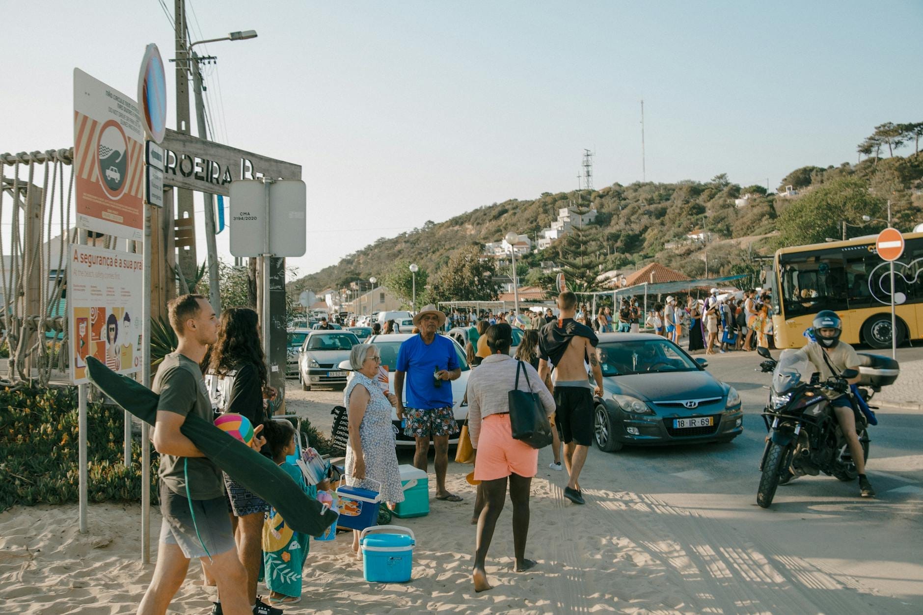 Menschenmassen mit Strandausrüstung und starkem Verkehr in der Nähe eines belebten Strandzugangs in Sardinien im Sommer.