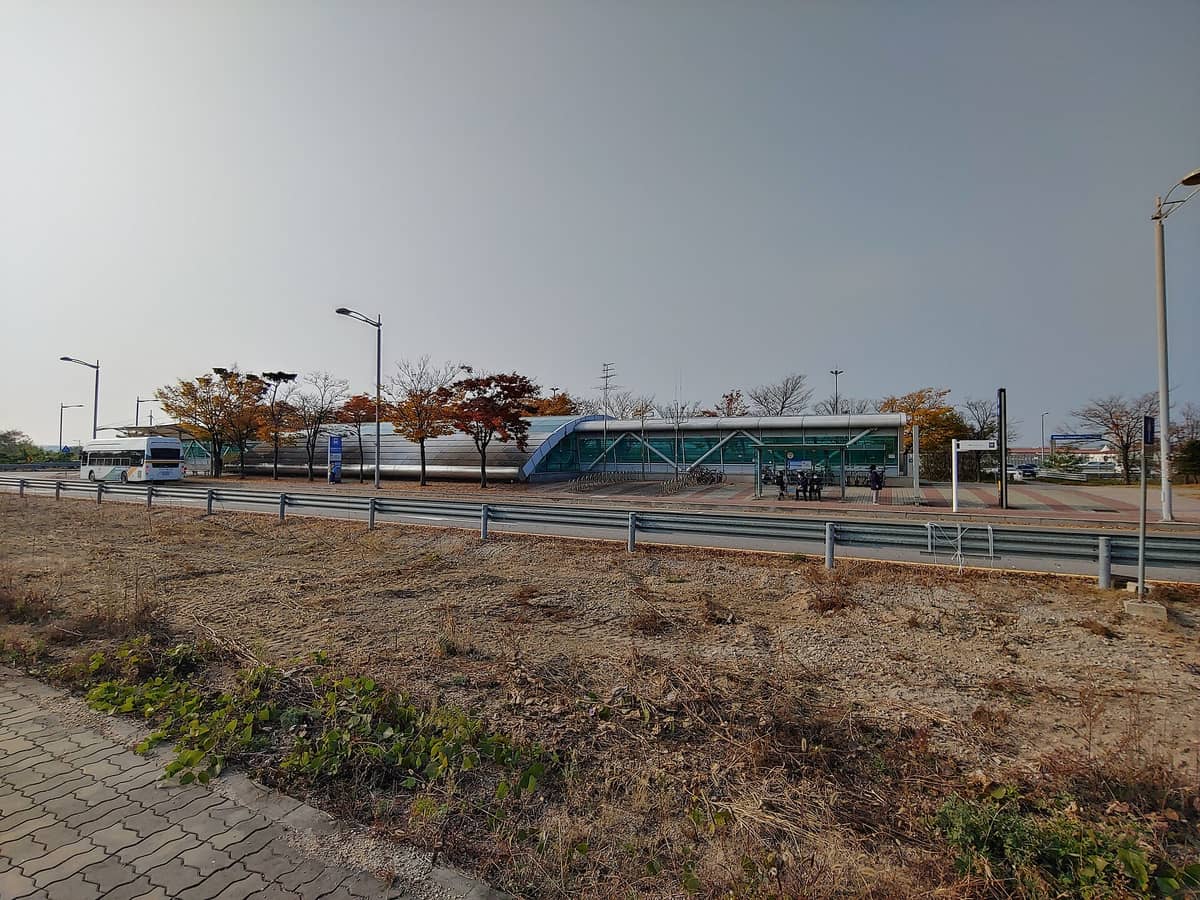 Vista ampla do exterior do Centro de Transporte do Aeroporto de Incheon, com um ônibus e árvores de outono, mostrando as instalações de transporte do aeroporto para Seul.