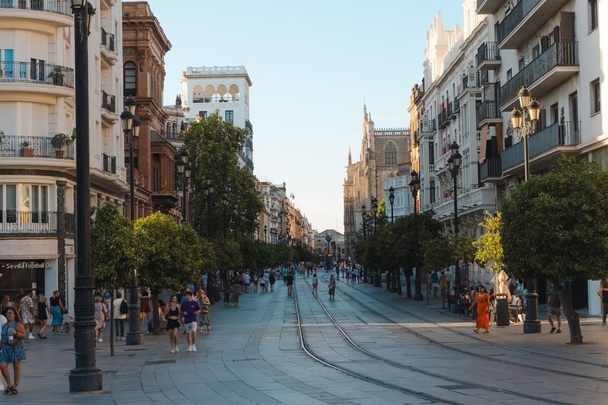 ถนนคนเดินกว้างในย่านประวัติศาสตร์ของเมือง Seville พร้อมราง Tram ผู้คนเดินเล่น อาคารประวัติศาสตร์ และมหาวิหารที่มองเห็นได้ในพื้นหลัง