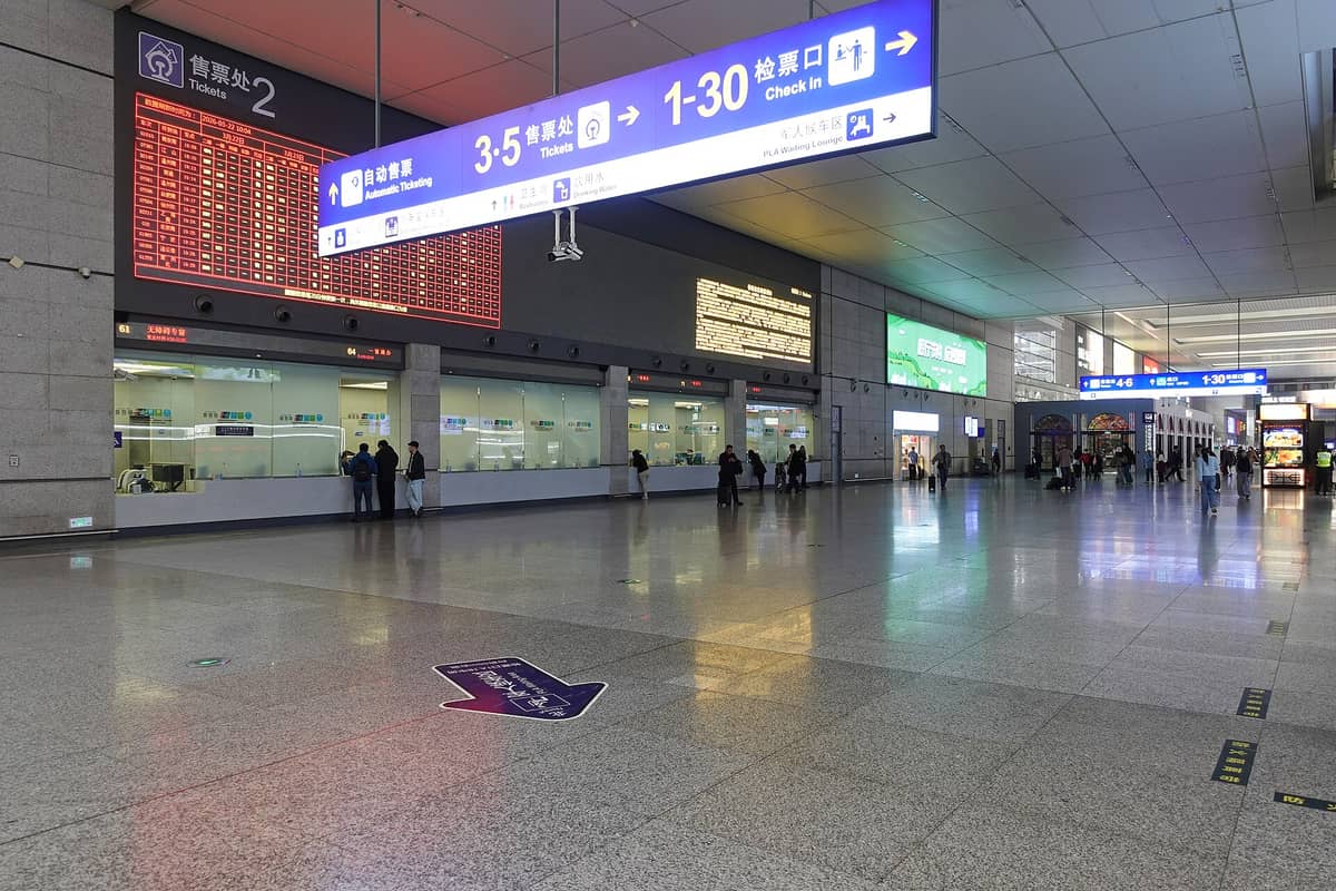 Tickethalle und Check-in-Bereich des Bahnhofs Shanghai Hongqiao mit digitalen Anzeigetafeln, Ticketschaltern und Reisenden in einem modernen Terminal.
