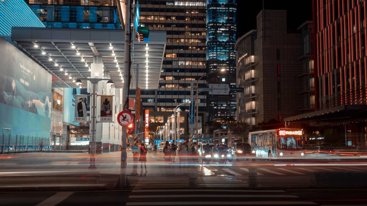 Rua urbana noturna em Shenzhen com ônibus, táxis e luzes brilhantes rodeada de altos edifícios modernos.