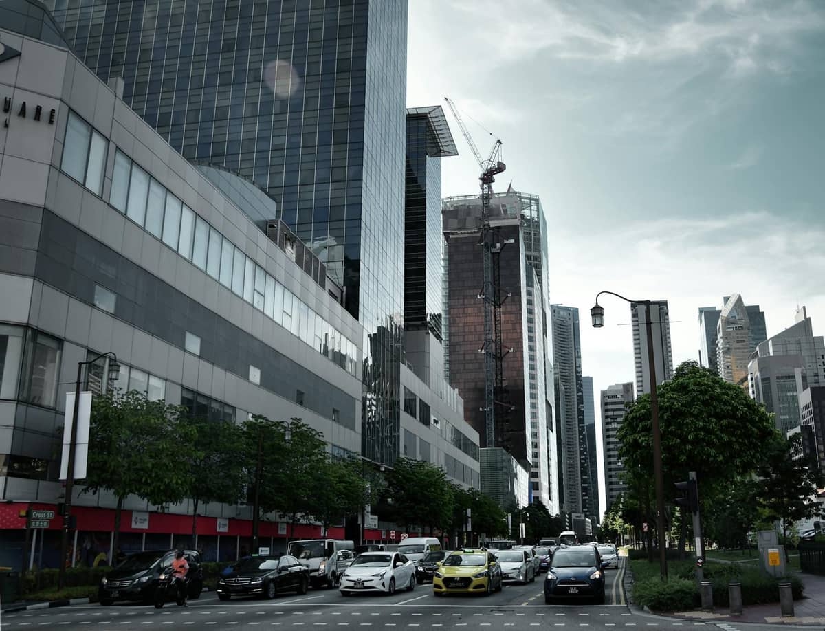 City street in Singapore with modern buildings and a yellow taxi among other cars driving, illustrating urban transport.