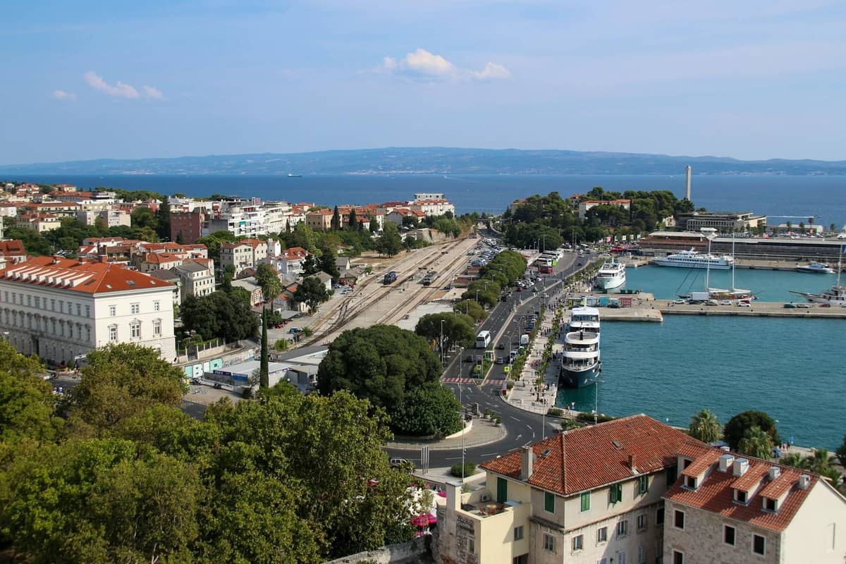 Luftaufnahme von Split mit den Bahngleisen, dem Busbahnhof und dem Fährhafen neben der Adria, die wichtige Transportmöglichkeiten hervorhebt.