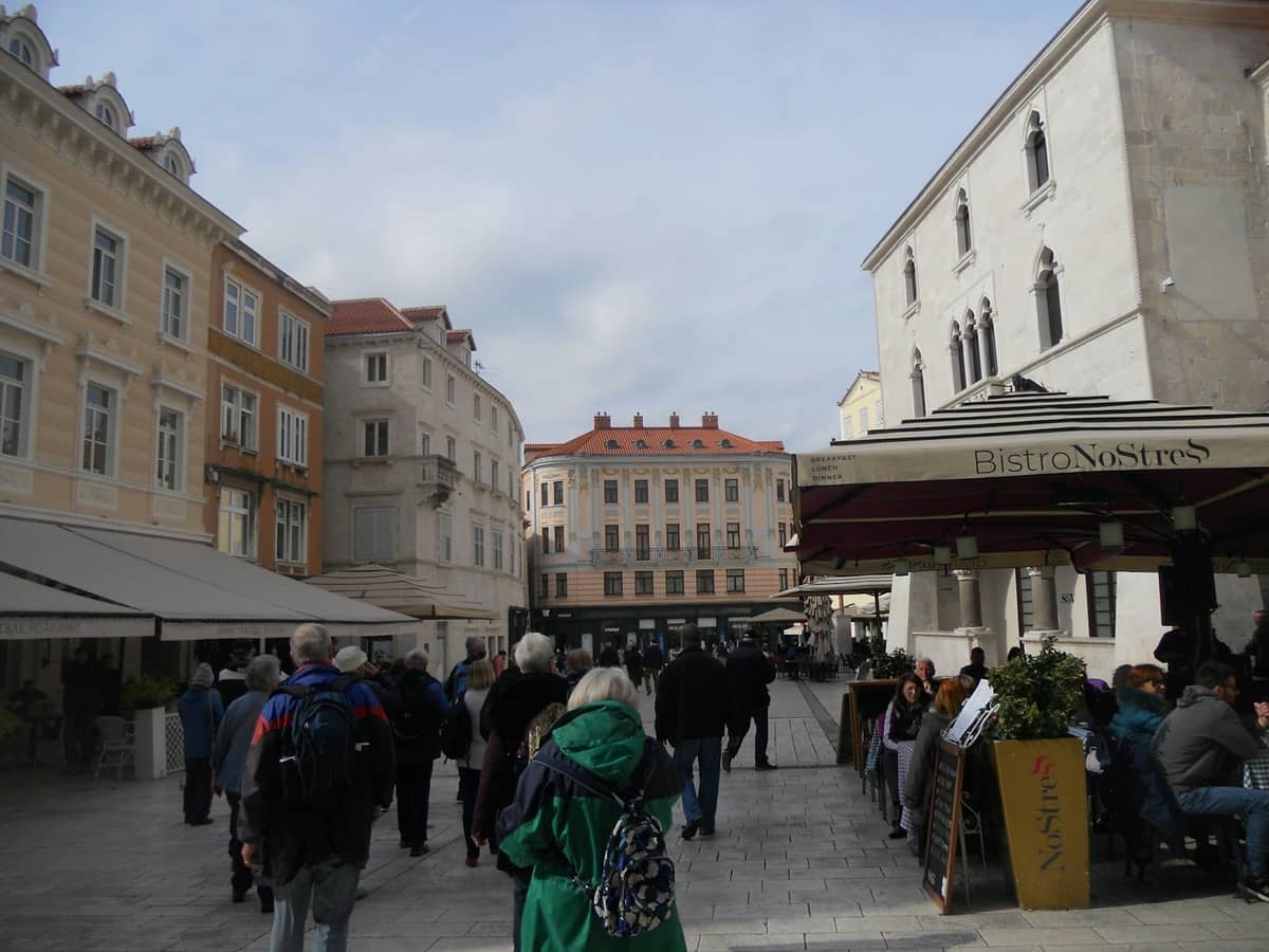 Touristen schlendern über einen gepflasterten Platz, gesäumt von historischen Gebäuden und Cafés im Zentrum von Split, Kroatien.