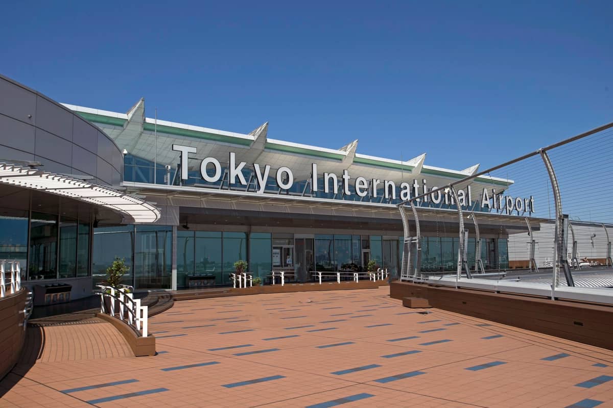 Exterior view of Haneda Tokyo International Airport terminal with large sign, clear sky, and observation deck in foreground.
