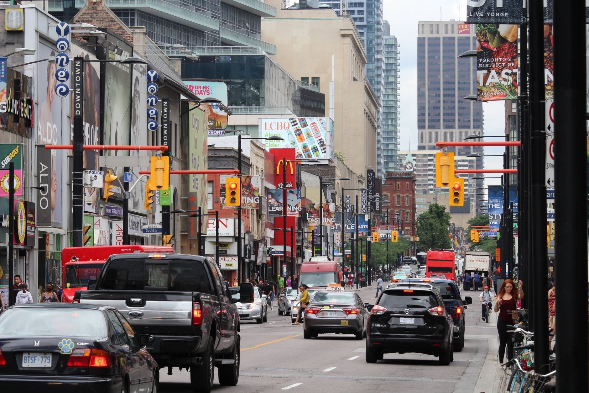 Vista movimentada da Yonge Street no centro de Toronto com carros, lojas, letreiros e pessoas nas calçadas.