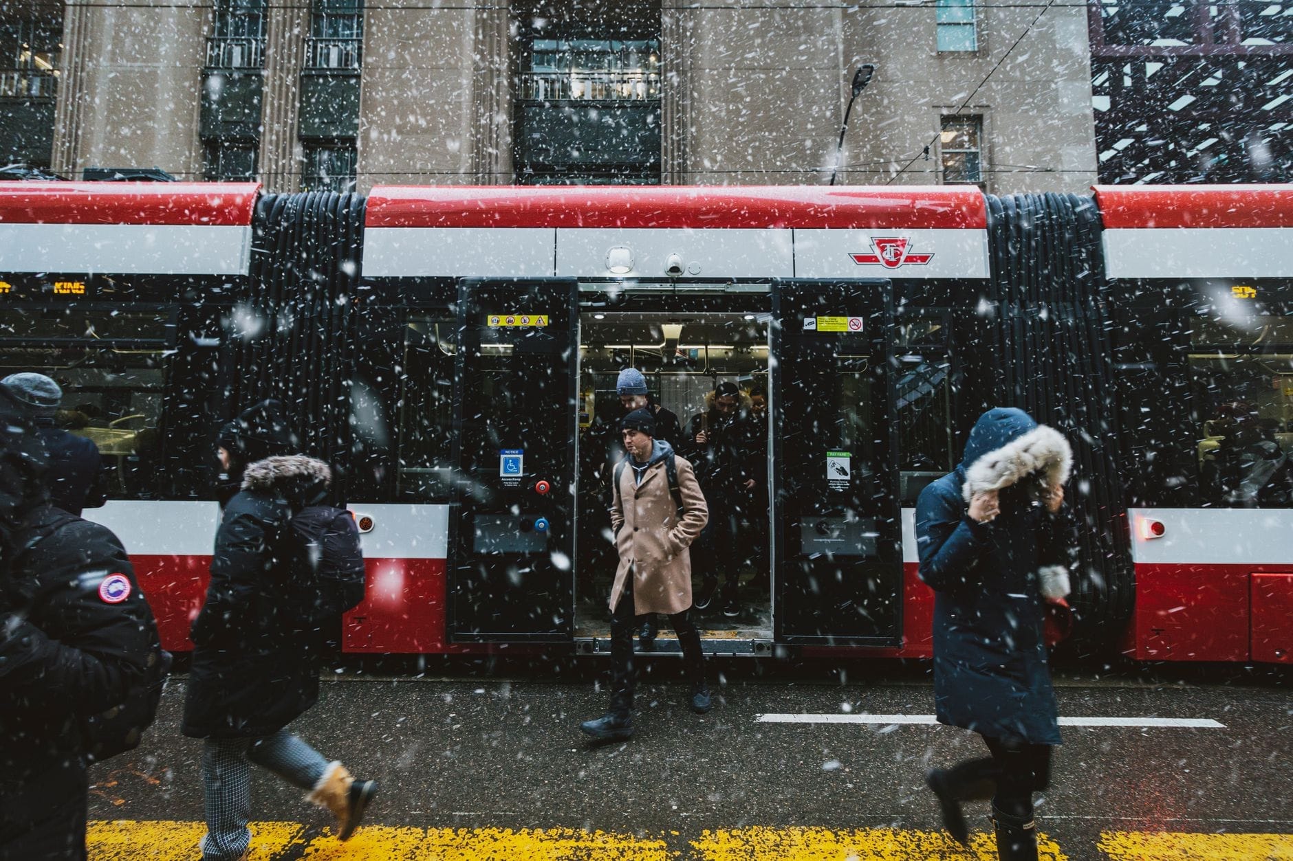 Pessoas saindo e embarcando em um bonde da TTC no centro de Toronto durante uma nevasca, com as cores vermelhas e brancas do transporte público.