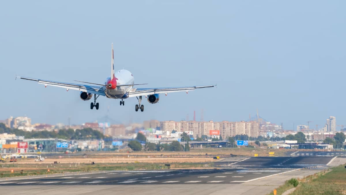 Un avión de pasajeros aterrizando en una pista con los edificios de Valencia visibles a lo lejos.