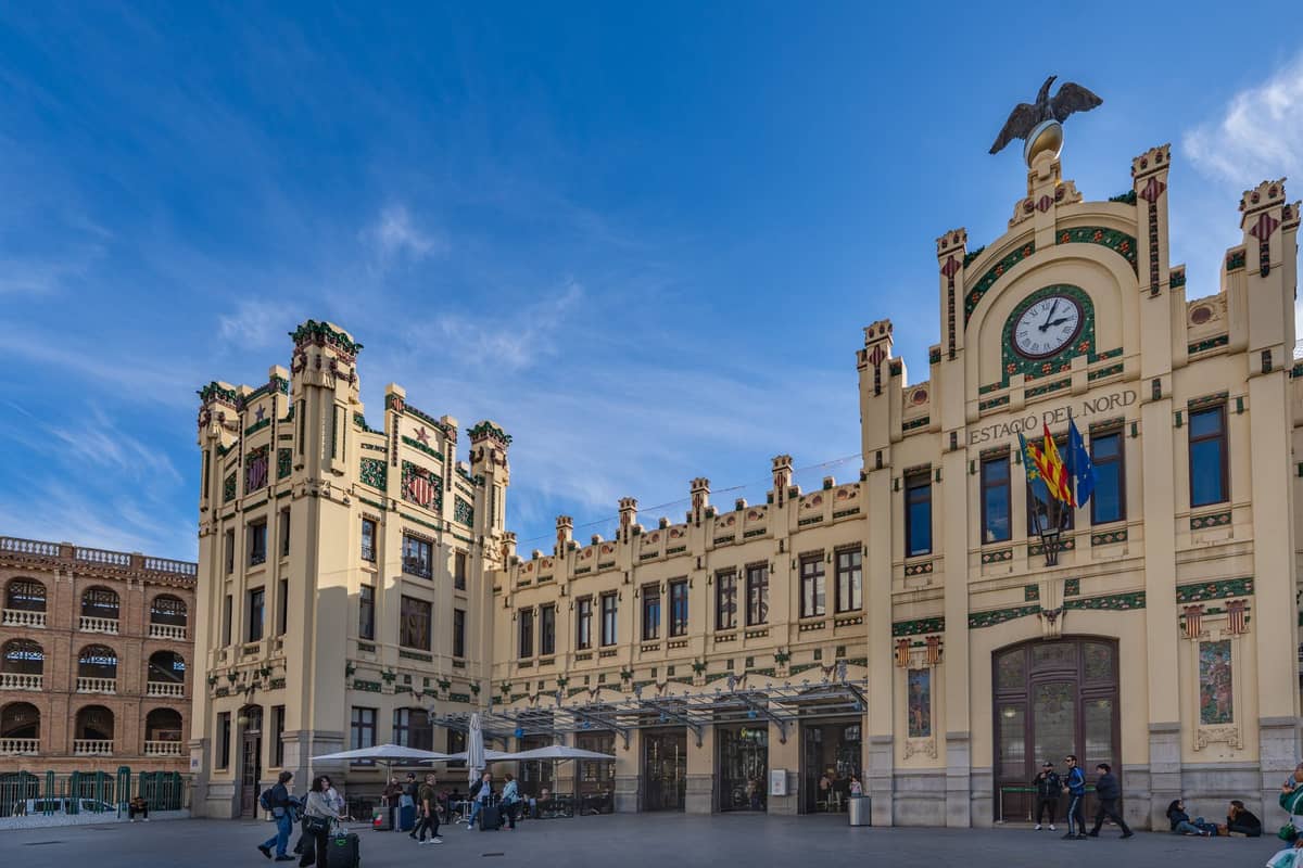 Vista amplia de la estación de tren Estació del Nord en Valencia, España, con personas fuera y señalización clara, bajo un cielo azul.