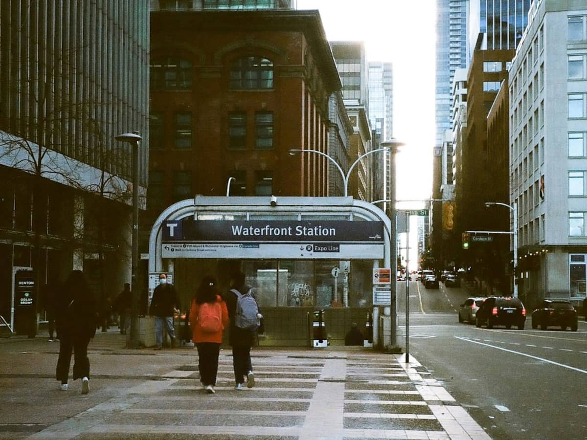 Menschen, die am Eingang der Waterfront Station in der Innenstadt von Vancouver vorbeigehen, umgeben von städtischen Gebäuden und Straßengeschehen.